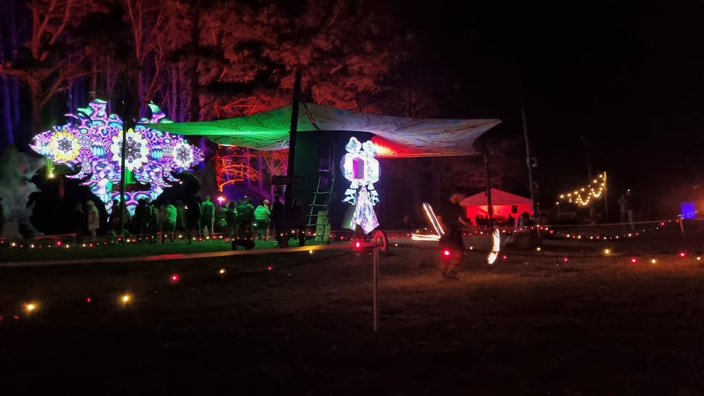 A vibrant photo capturing a ravers and a fire dancer and a rave in a lush rural bush setting