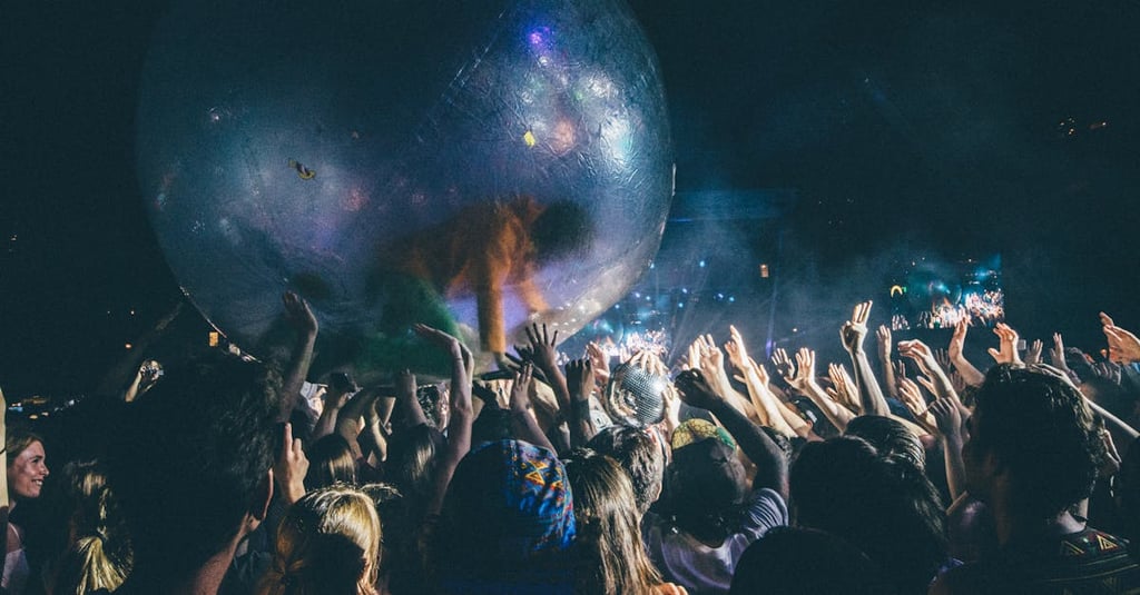 Vibrant night concert scene with crowd interaction and giant inflatable ball under dynamic lighting.